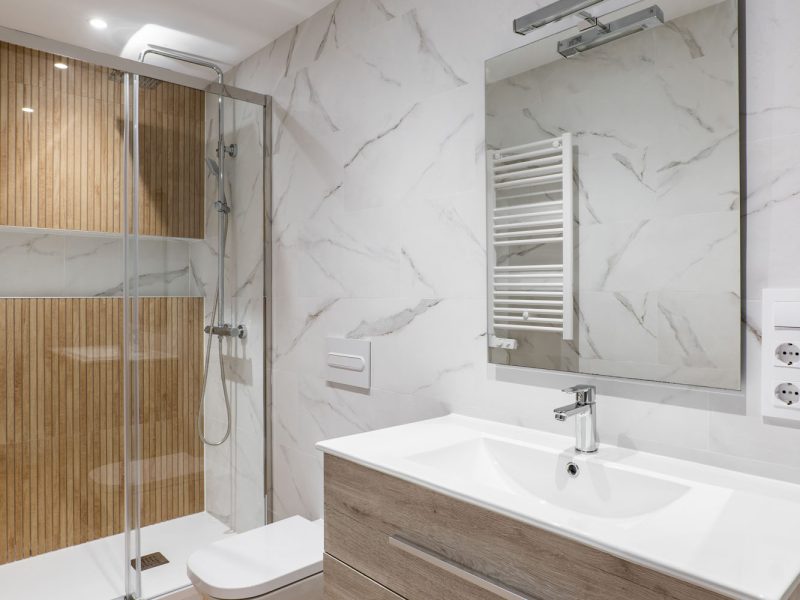 Simple and modern bathroom with marble white tiles, wooden finishing, toilet and shower.